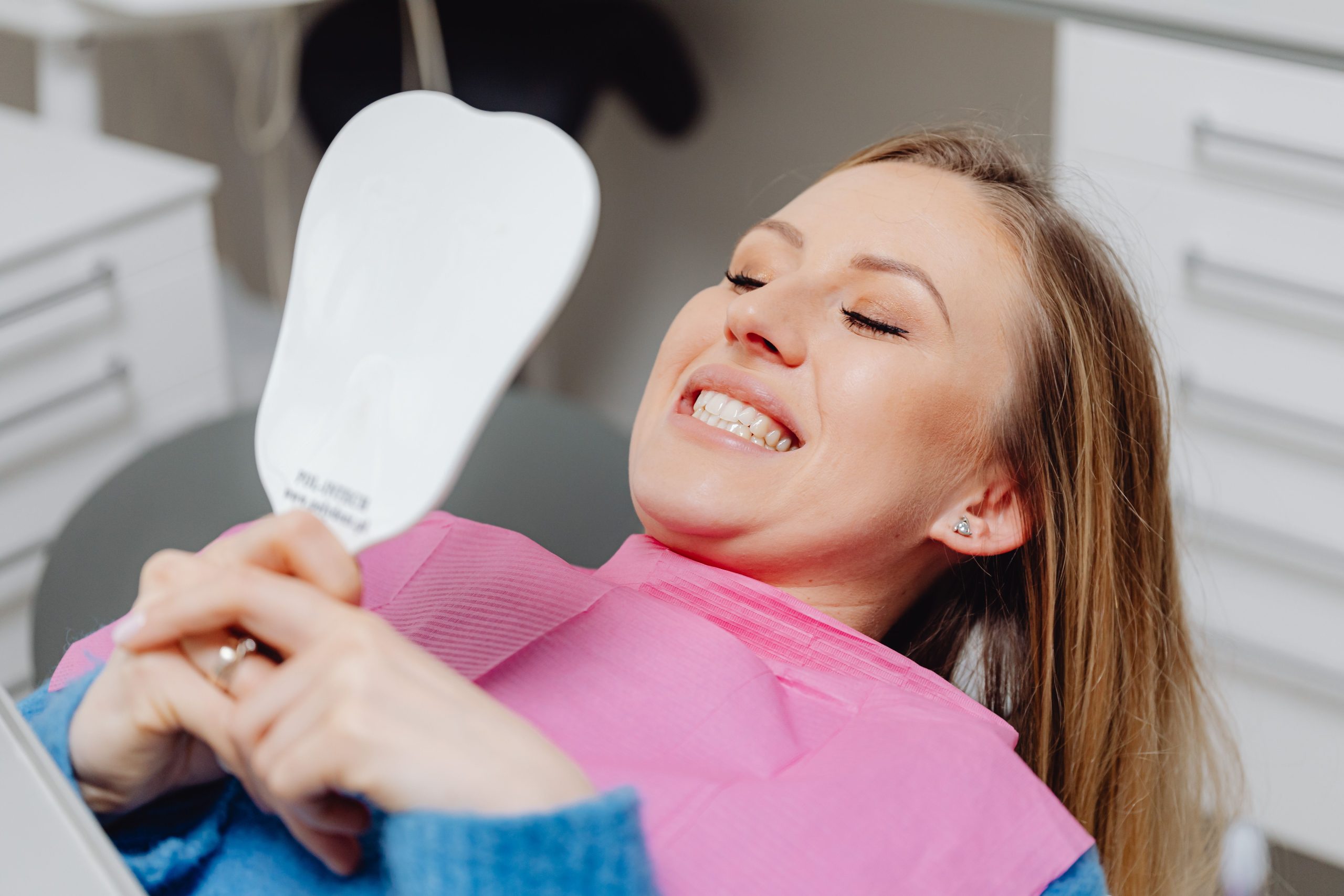 Femme souriant devant un miroir après son traitement dentaire